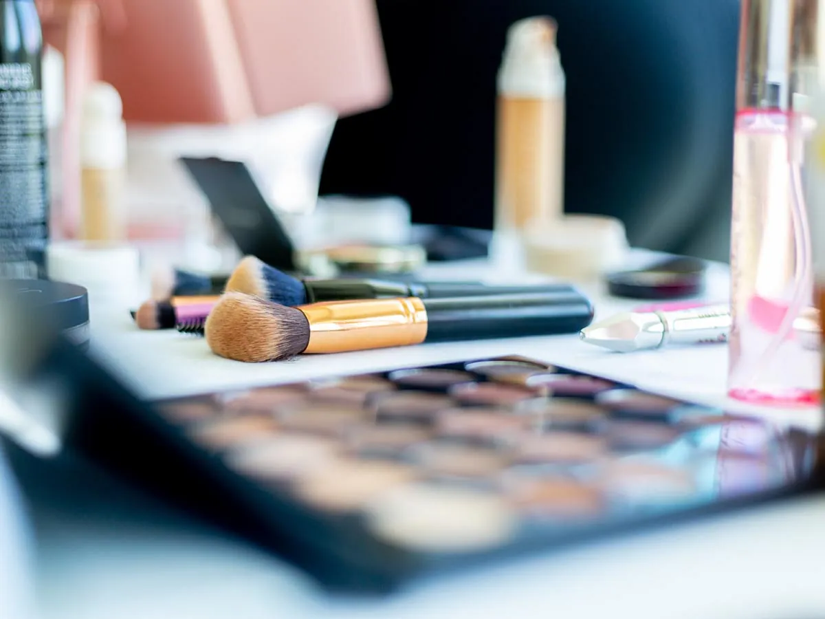 Make Up Pinsel und Lidschattenpalette auf einem Tisch zusammen mit anderen Make Up Produkten